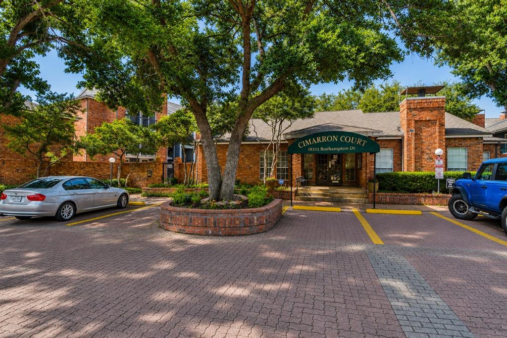 18333 Roehampton Drive, Unit 1036 Dallas, TX 75252 - Photo 12 of 12 Brick facade building with a prominent entrance featuring a green awning, surrounded by mature trees