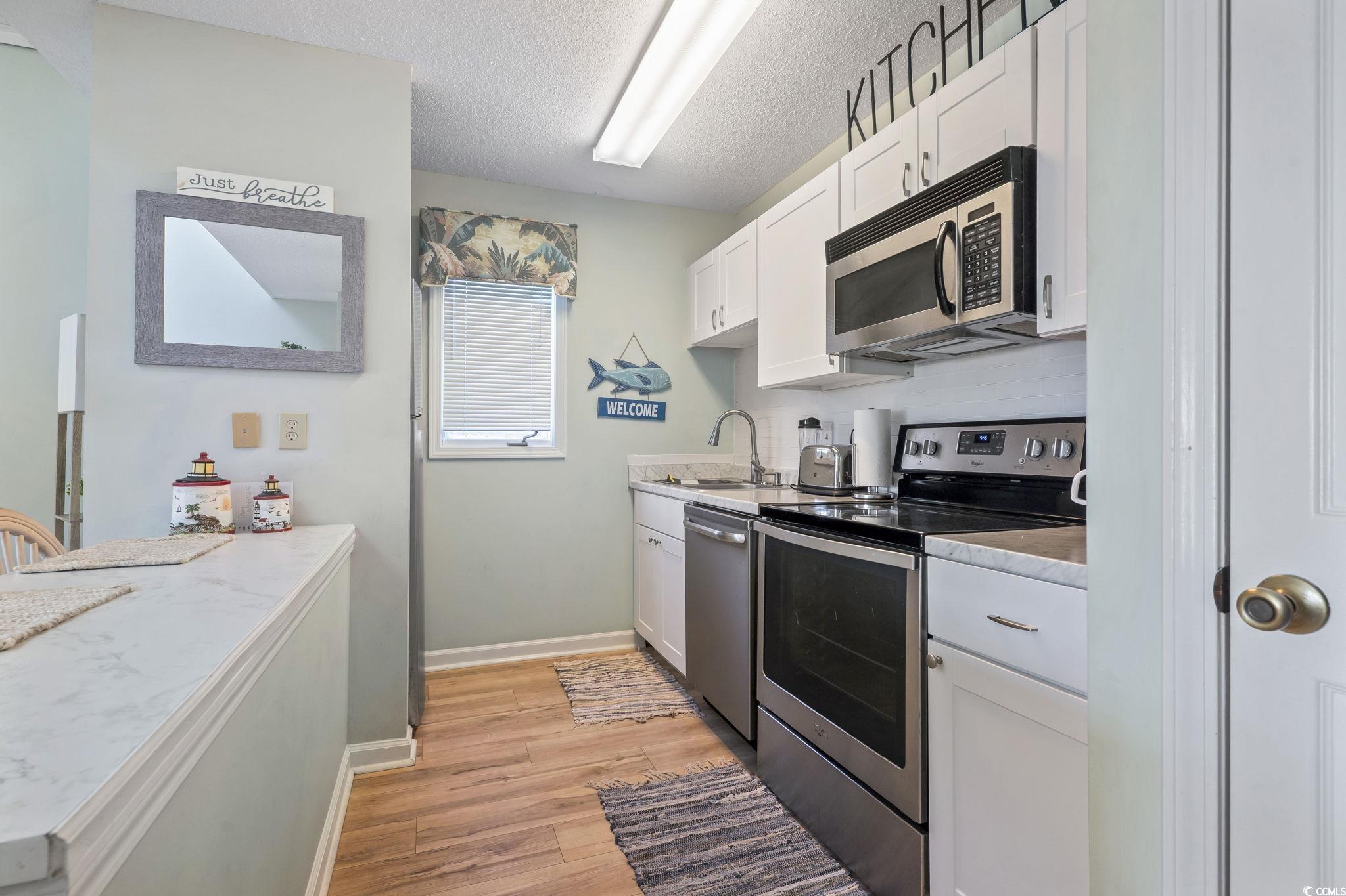 207 Double Eagle Drive, Unit F3 Myrtle Beach, SC 29575 - Photo 13 of 40 Kitchen featuring appliances with stainless steel finishes, white cabinets, light countertops, a textured ceiling, and light wood-style floors