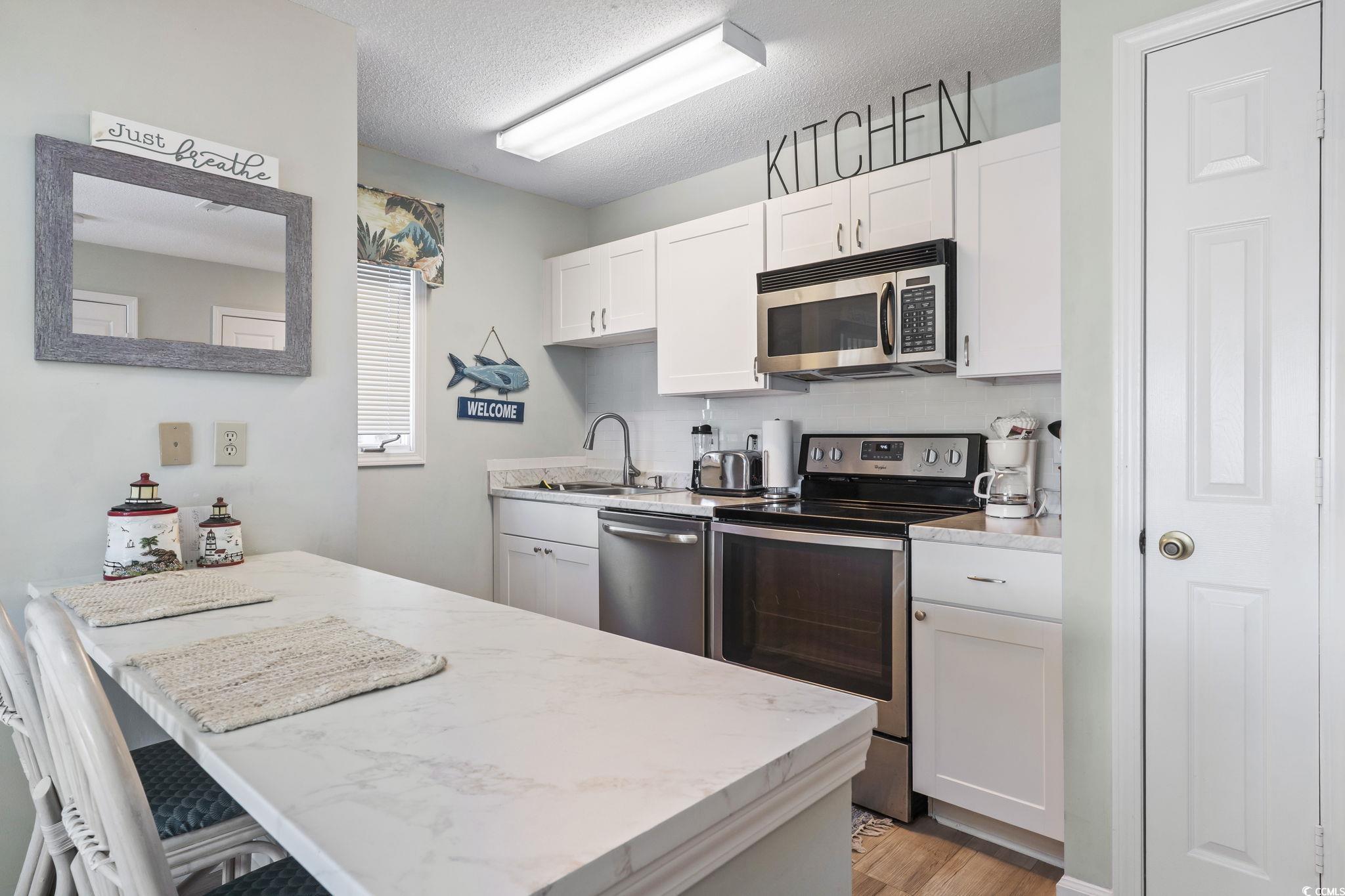 207 Double Eagle Drive, Unit F3 Myrtle Beach, SC 29575 - Photo 16 of 40 Kitchen with stainless steel appliances, white cabinets, a textured ceiling, a peninsula, and a kitchen breakfast bar