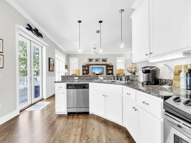 a kitchen with stainless steel appliances granite countertop a stove a sink dishwasher a refrigerator white cabinets and wooden floor next to a window