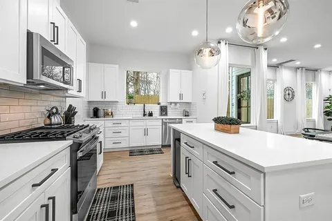 a kitchen with a sink dishwasher a stove a refrigerator and white cabinets with wooden floor