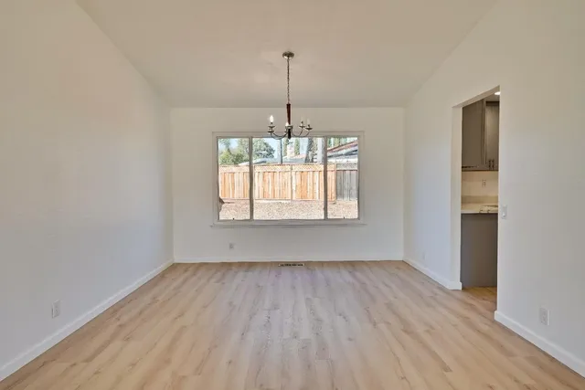 a view of a room with wooden floor chandelier and a kitchen
