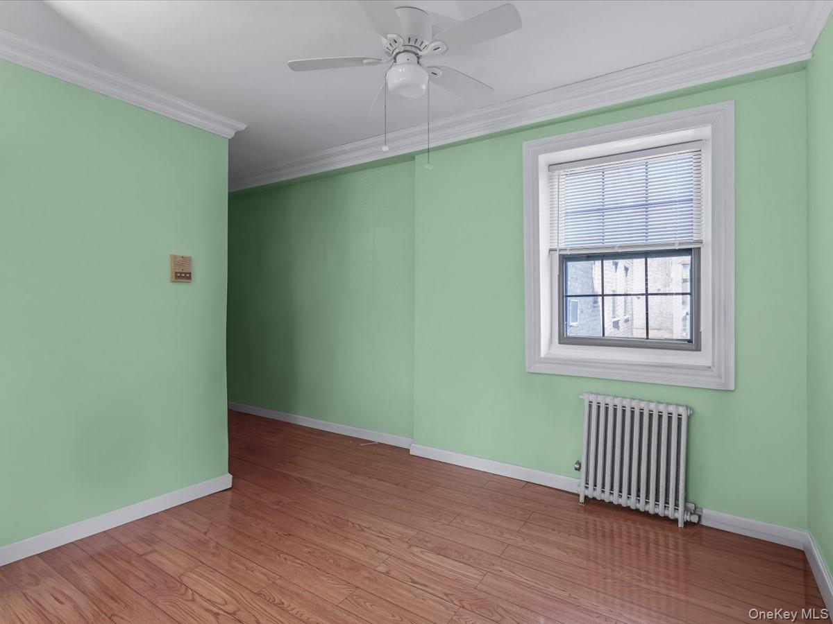 147-11 79th Avenue, Unit 1N Queens, NY 11367 - Photo 2 of 8 Empty room featuring radiator, ornamental molding, wood finished floors, and ceiling fan