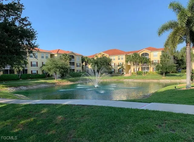 a view of a fountain in front of a big yard with plants and large trees