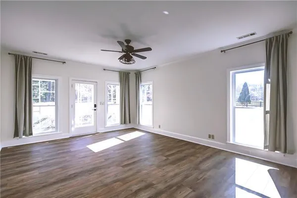 an empty room with wooden floor chandelier fan and windows