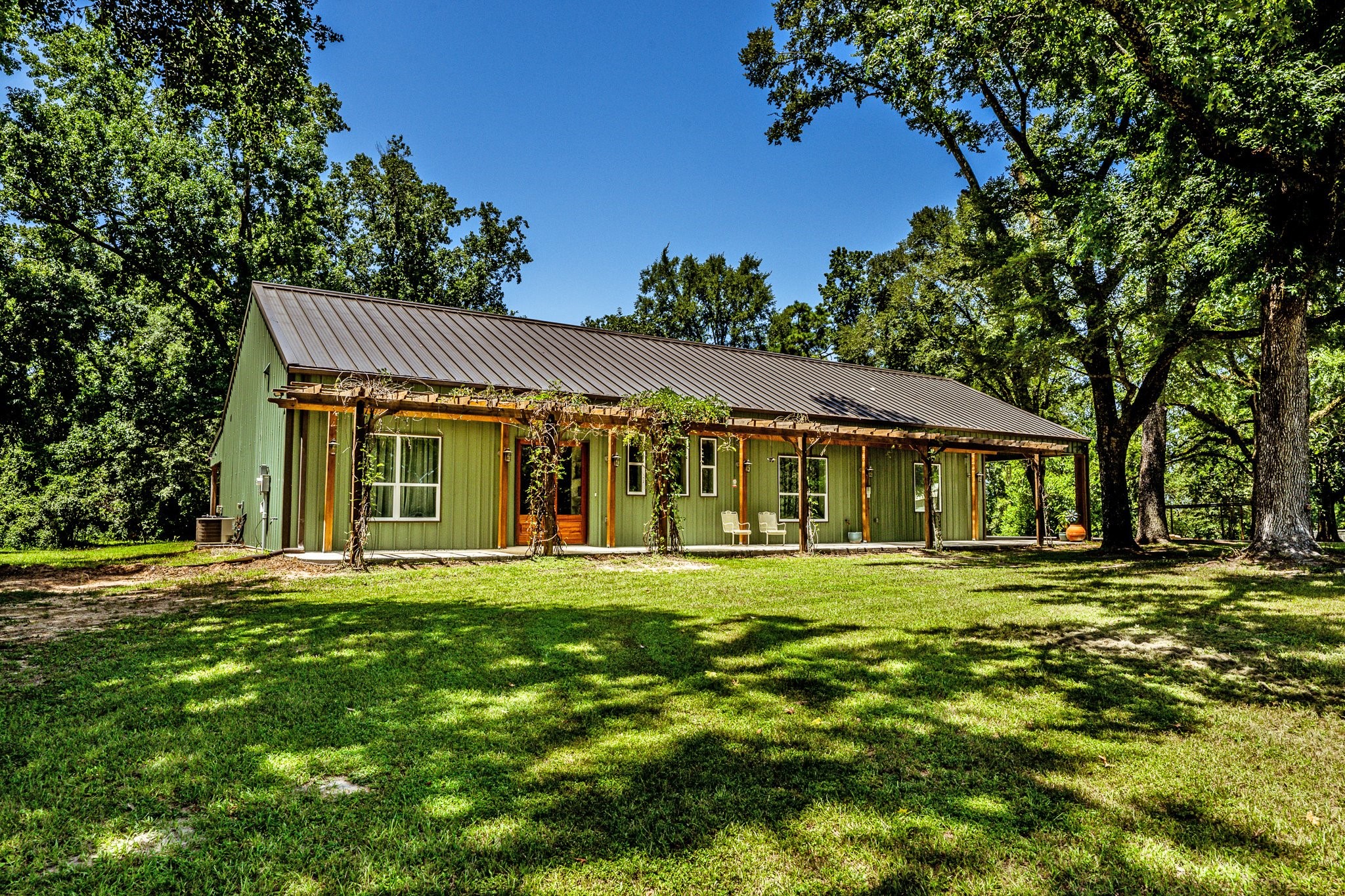 Nestled under a canopy of mature trees, this custom barndominium-style home blends rustic charm with modern design.