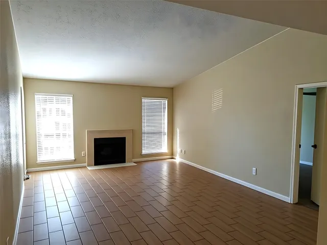 an empty room with windows fireplace and wooden floor