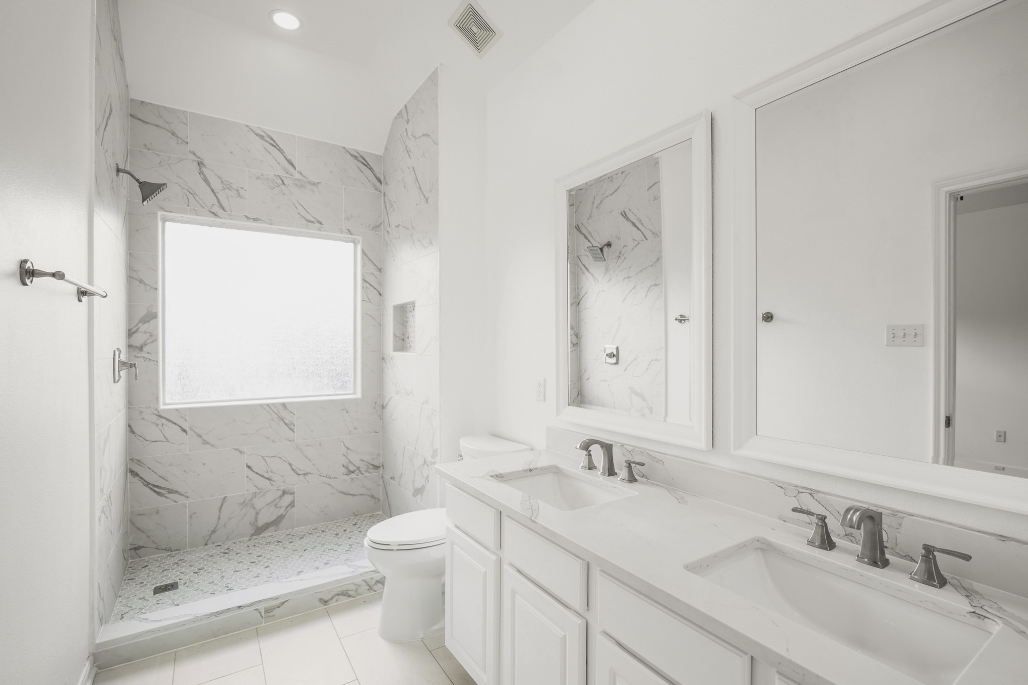 21810 Mansfield Bluff Lane Spring, TX 77379 - Photo 18 of 34 Inside the primary bath, the remodeled space features a dual-sink vanity with two framed mirrors and updated finishes. An oversized walk-in shower sits just beyond, with a window bringing in natural light.
