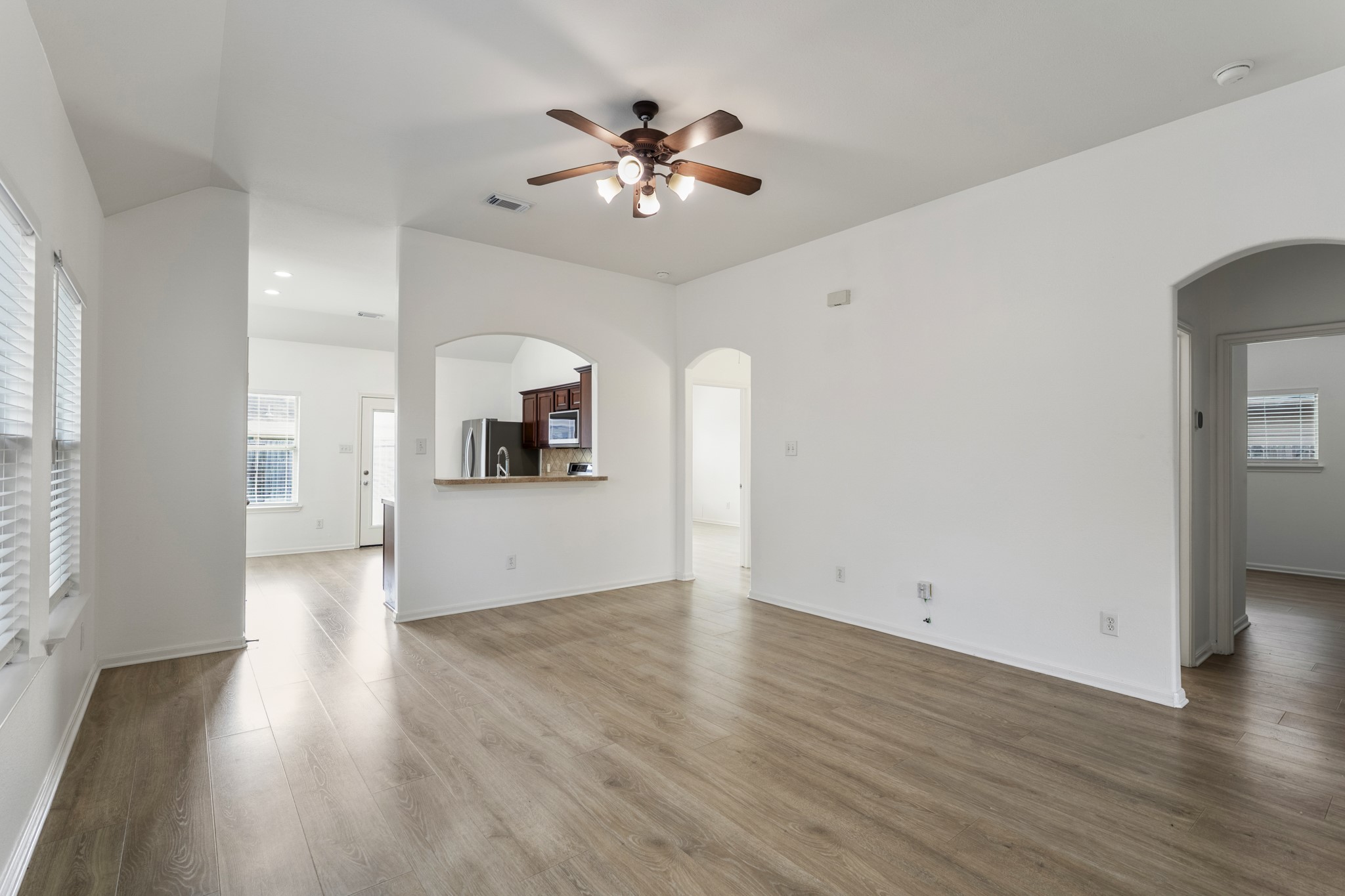 21810 Mansfield Bluff Lane Spring, TX 77379 - Photo 5 of 34 Moving into the living area, the space opens up with vaulted ceilings and a ceiling fan overhead, while vinyl plank flooring continues throughout. From here, the kitchen and breakfast area are fully in view, keeping everything connected. The doorway to the right leads to the secondary bedrooms, while just before the kitchen, another doorway on the right leads to the primary bedroom and laundry room.