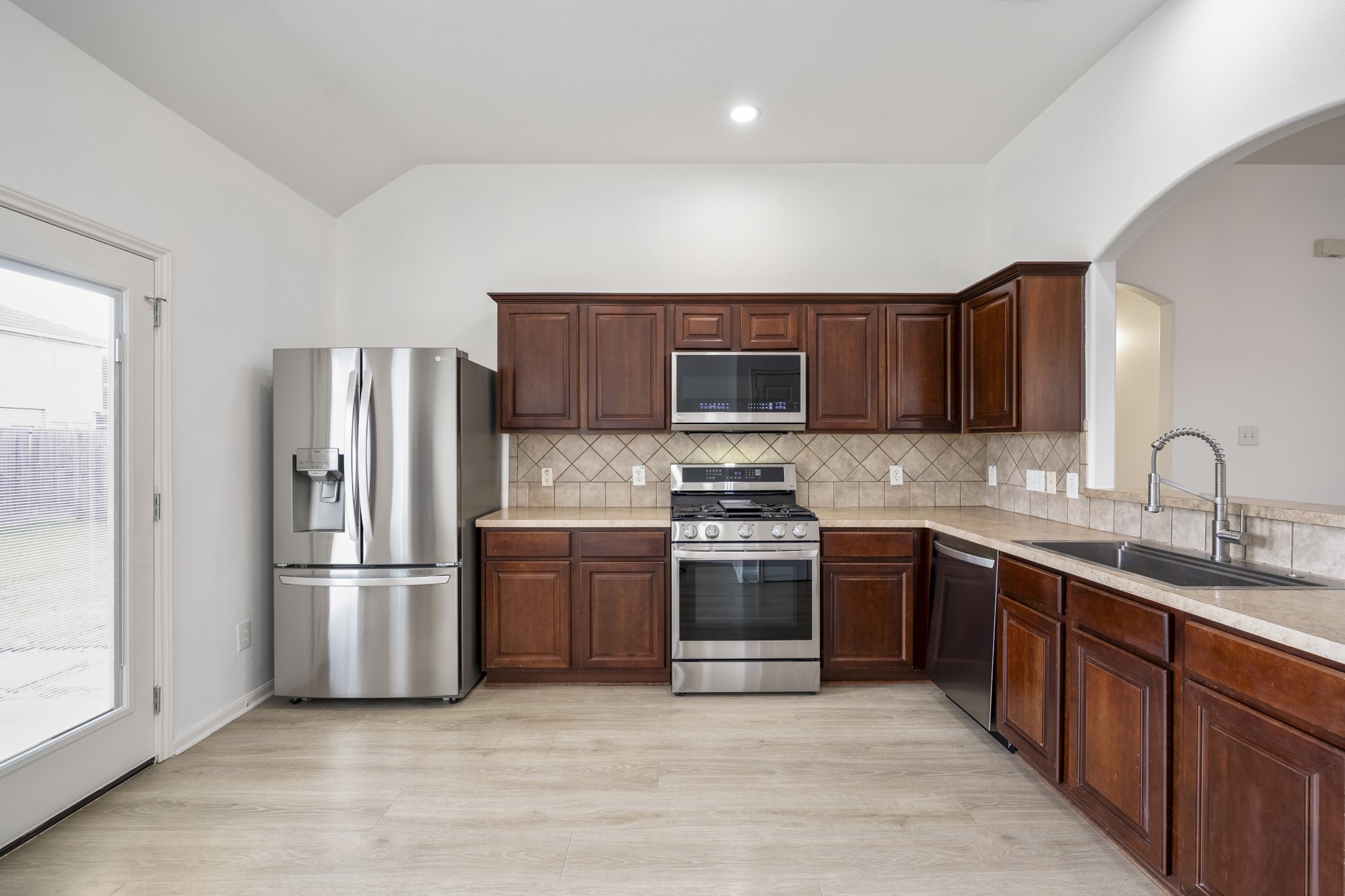 21810 Mansfield Bluff Lane Spring, TX 77379 - Photo 8 of 34 From this angle, the kitchen shows off its full layout with stainless steel appliances, including a gas range, built-in microwave, dishwasher, and refrigerator. A long stretch of counter space and cabinetry lines one side, with the pantry just off to the left, keeping storage and everyday functionality within easy reach.