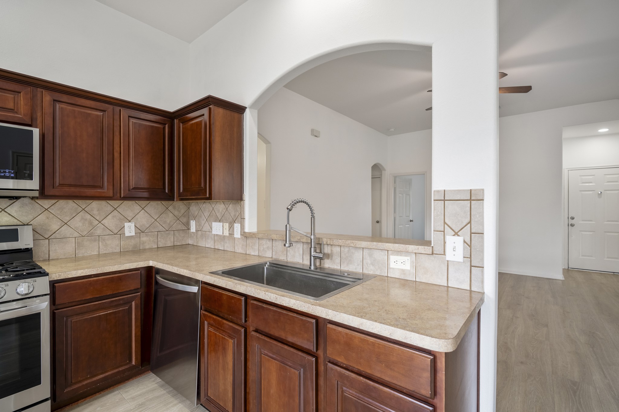 21810 Mansfield Bluff Lane Spring, TX 77379 - Photo 10 of 34 A closer look at the sink area highlights the single-basin stainless steel sink with pull-down sprayer faucet, set into a stretch of counter space that keeps prep and cleanup easy. Above, the arched opening looks back into the living area, keeping the connection between spaces open and in view.