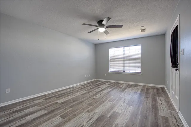 a view of an empty room with wooden floor and a ceiling fan