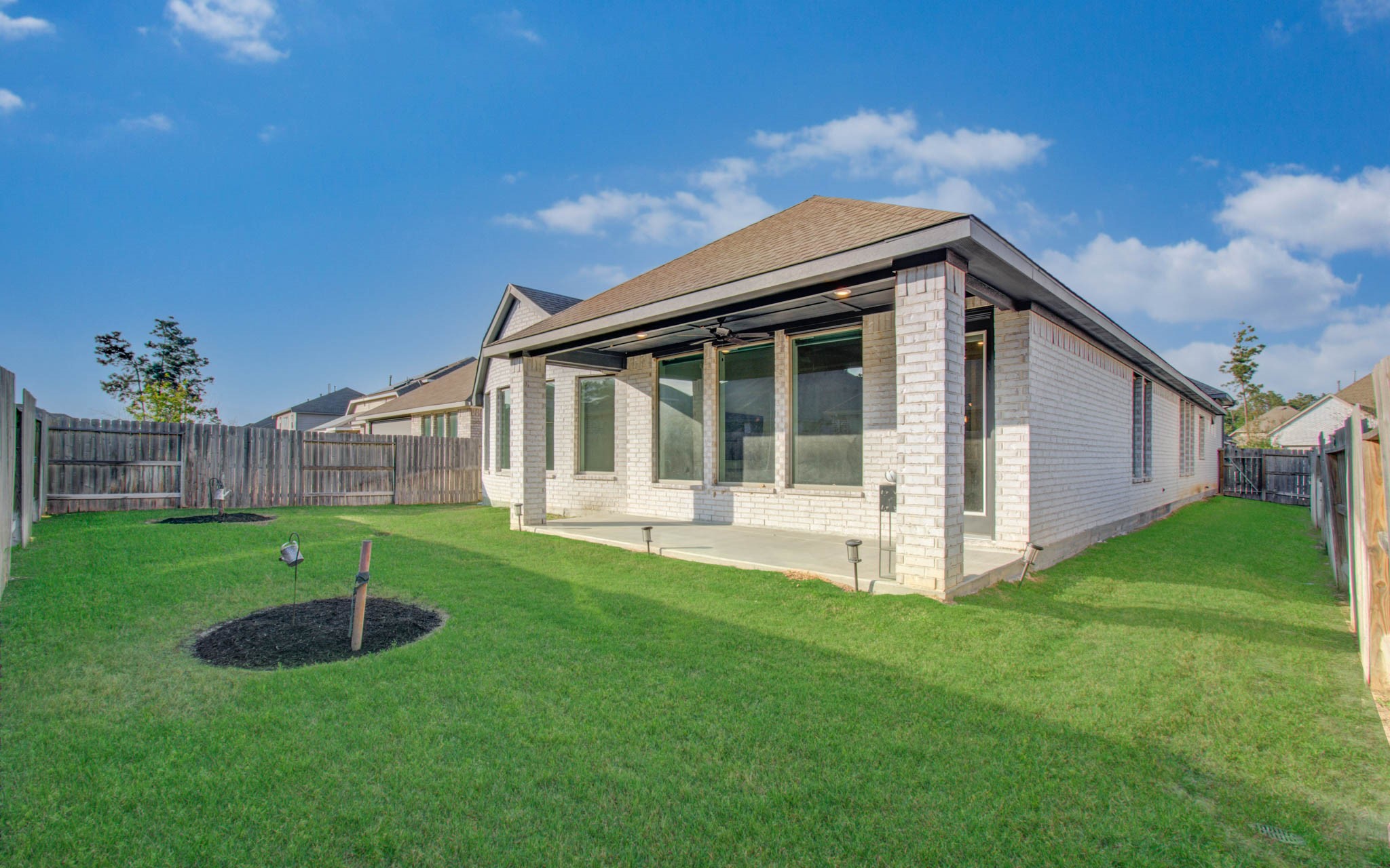 17344 Grand Canyon Road Conroe, TX 77302 - Photo 47 of 49 This photo shows a modern brick home with a spacious backyard. The yard is well-maintained with lush green grass, a small landscaped area, and a covered patio, perfect for outdoor relaxation.