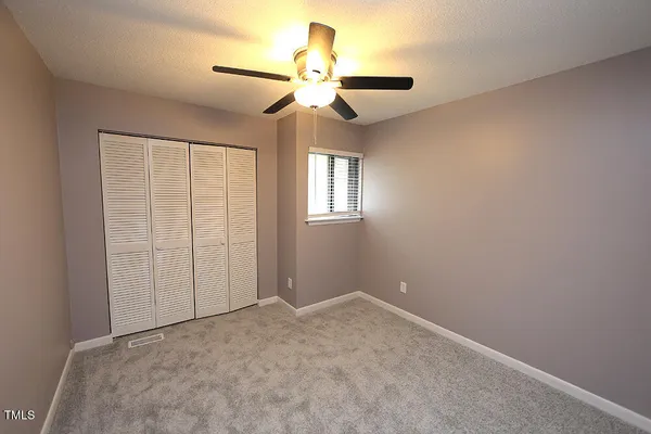an empty room with a chandelier fan and windows