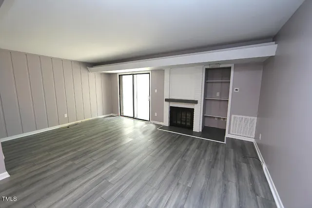 an empty room with wooden floor fireplace and windows