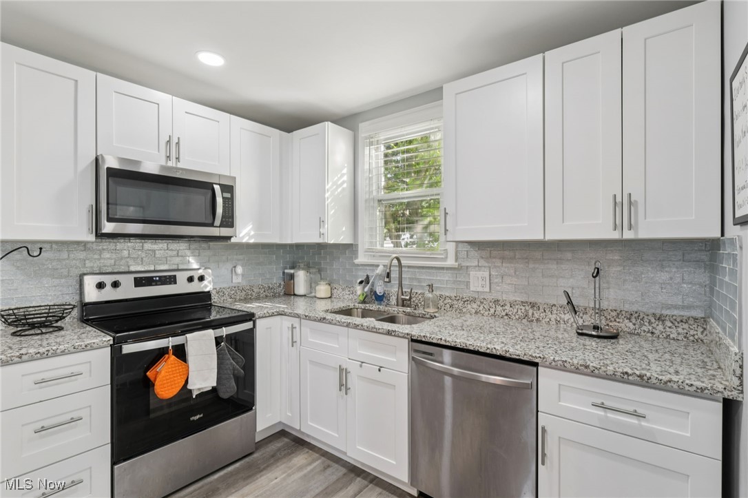 1503 Oakmount Road South Euclid, OH 44121 - Photo 22 of 50 Kitchen featuring stainless steel appliances, white cabinets, light stone countertops, light wood-type flooring, and backsplash