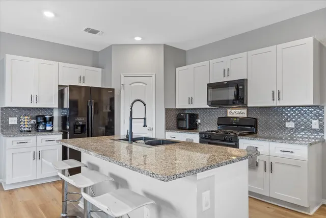 a kitchen with stainless steel appliances granite countertop a sink stove refrigerator and white cabinets with wooden floor