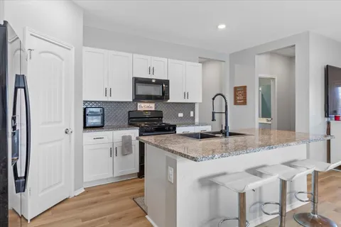 a kitchen with stainless steel appliances granite countertop a sink stove refrigerator and white cabinets with wooden floor