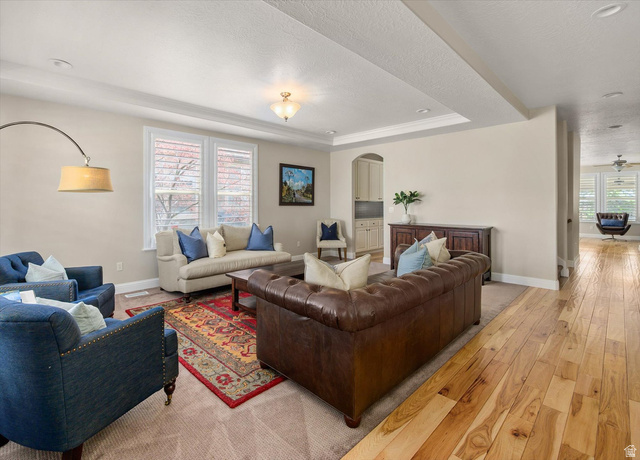 1456 Firelight Way Sandy, UT 84092 - Photo 5 of 22 Living room with light wood finished floors, arched walkways, a textured ceiling, and a tray ceiling