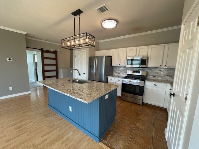 Kitchen featuring a large island with a stone countertop and integrated sink, stainless steel appliances, white cabinetry with dark hardware, a tiled backsplash, and recessed lighting