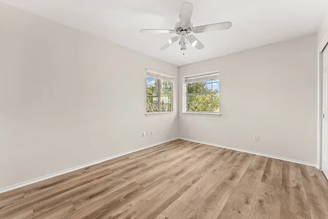 an empty room with wooden floor chandelier fan and windows