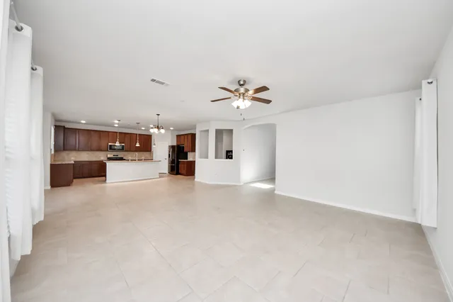 an empty room with chandelier fan and windows