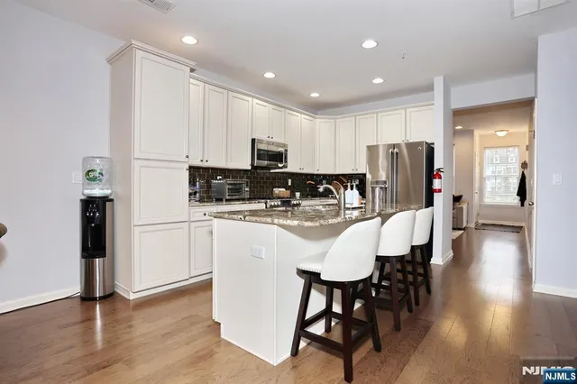 a kitchen with stainless steel appliances granite countertop a refrigerator a stove a sink a dining table and chairs with wooden floor