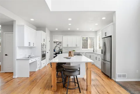 a kitchen with a sink a refrigerator and white cabinets with wooden floor