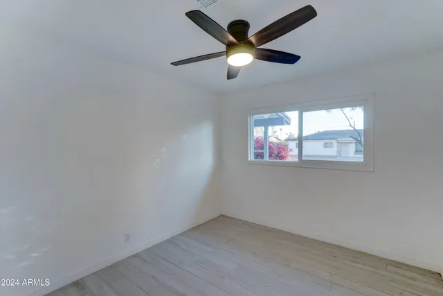 an empty room with wooden floor ceiling fan and window