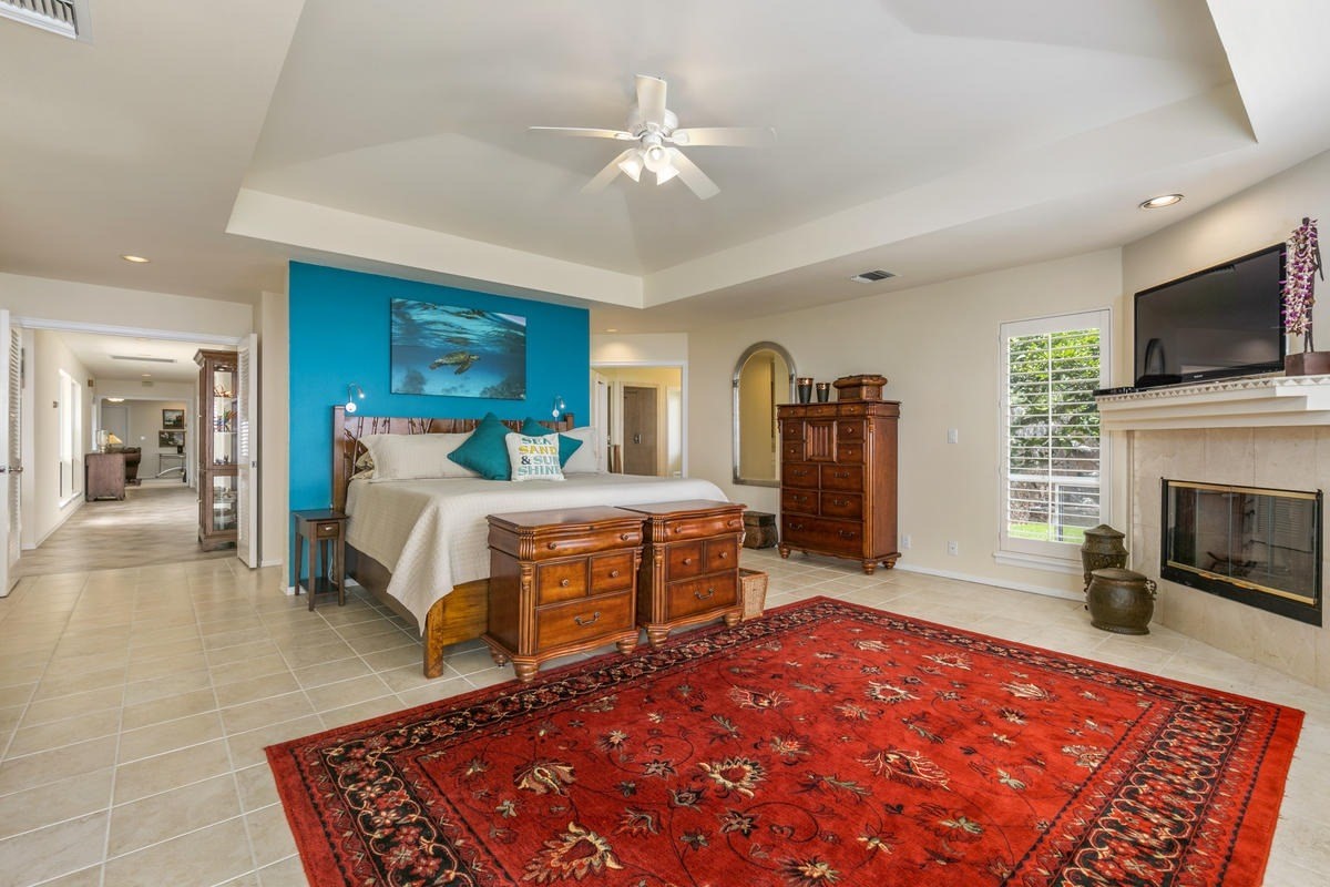 59-1764 Kohala Ranch Road Kamuela, HI 96743 - Photo 20 of 30 a bedroom with a large bed a flat tv screen and a fireplace