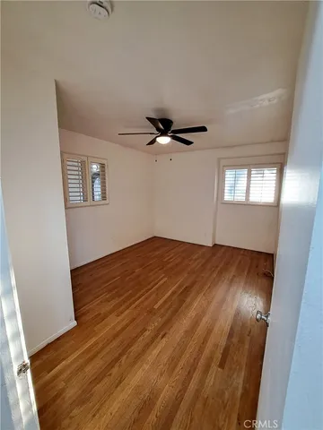an empty room with wooden floor fan and windows