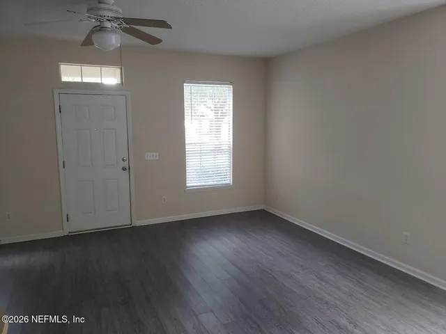 an empty room with wooden floor chandelier fan and windows