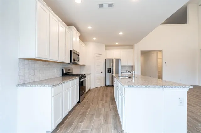 a large kitchen with stainless steel appliances granite countertop a lot of counter space and wooden floor