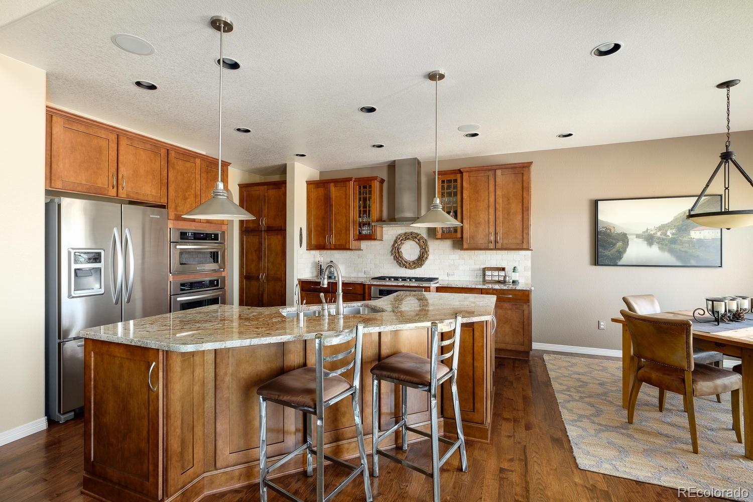 9367 Viaggio Way Highlands Ranch, CO 80126 - Photo 4 of 9 a kitchen with stainless steel appliances kitchen island granite countertop a refrigerator a stove top oven a sink dishwasher and white cabinets with wooden floor