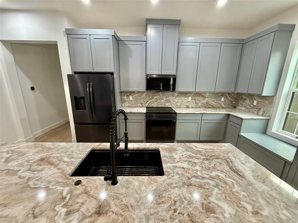 2936 Henry Road Lancaster, TX 75134 - Photo 7 of 28 Kitchen featuring a large island with a black basin sink and pull-down faucet, light gray cabinetry, built-in stainless steel appliances, a window with a built-in bench, and patterned countertops with matching backsplash