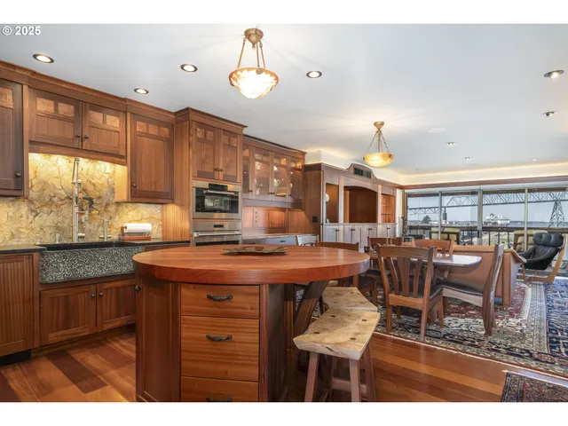 a room with stainless steel appliances kitchen island granite countertop a refrigerator a stove and a sink with wooden floor