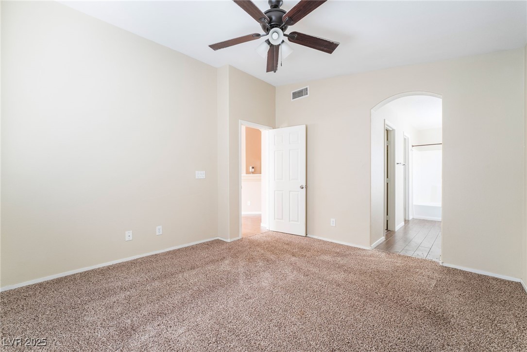1570 Rusty Ridge Lane Henderson, NV 89002 - Photo 23 of 35 Unfurnished room with arched walkways, a ceiling fan, visible vents, light carpet, and baseboards