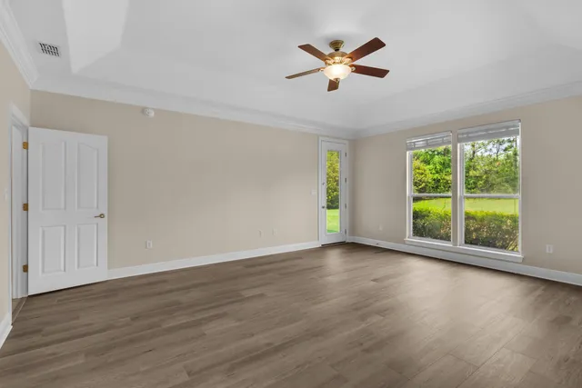 an empty room with wooden floor fan and windows