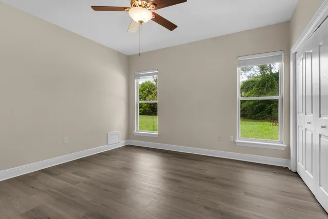 an empty room with wooden floor fan and windows