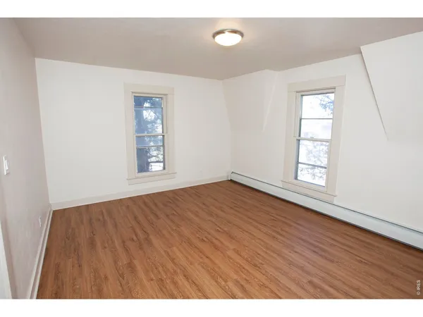 a view of an empty room with chandelier fan and wooden floor