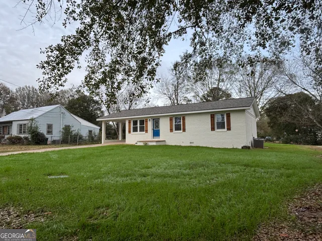 a house that is sitting in the grass with large trees and plants