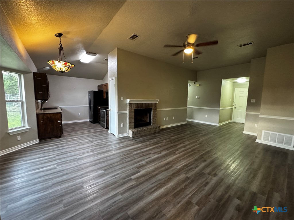 397 County Road 3367 Kempner, TX 76539 - Photo 8 of 47 an empty room with wooden floor a ceiling fan a kitchen view and a fireplace