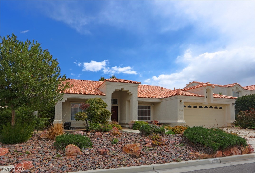 A charming stucco home with a terracotta tile roof features desert landscaping and a double garage.