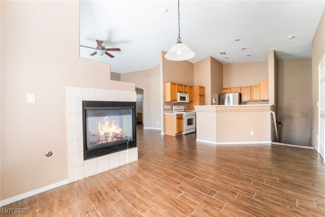 1570 Rusty Ridge Lane Henderson, NV 89002 - Photo 7 of 35 Unfurnished living room featuring ceiling fan, high vaulted ceiling, a tile fireplace, and wood finished floors