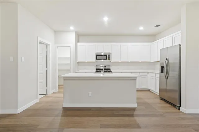 a view living room with stainless steel appliances granite countertop a refrigerator a sink and white cabinets with wooden floor
