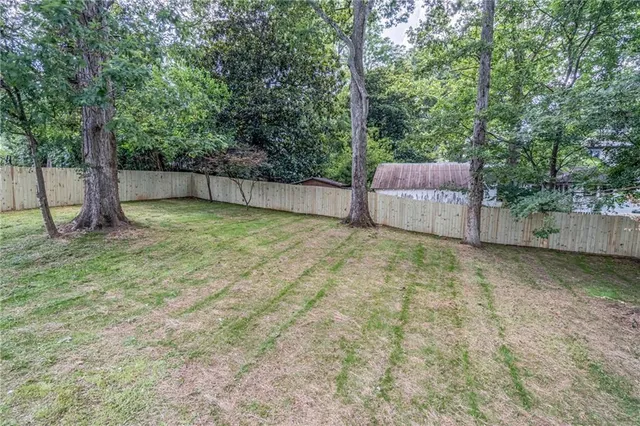 a view of a backyard with large trees and wooden fence