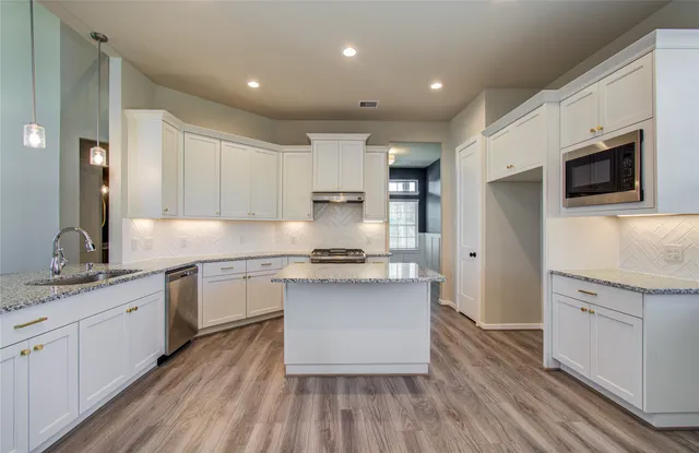 a kitchen with stainless steel appliances granite countertop a stove top oven a sink dishwasher and a refrigerator with wooden floor