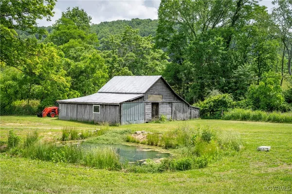 a house that is sitting in the grass with large trees and plants