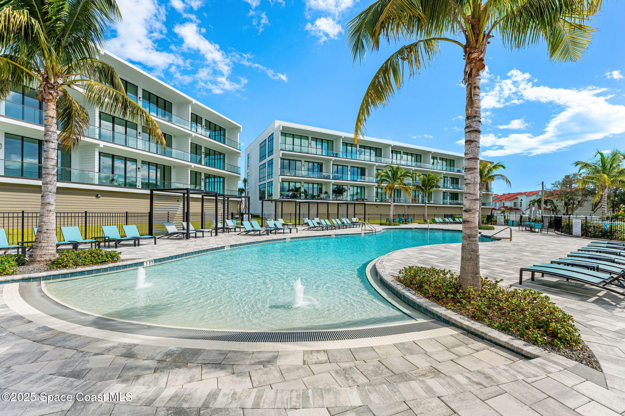 225 Strand Drive, Unit 401 Melbourne Beach, FL 32951 - Photo 42 of 51 a view of a swimming pool with a lawn chairs and palm tree