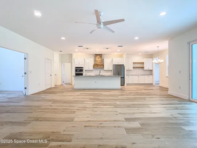 an empty room with wooden floor chandelier fan and windows
